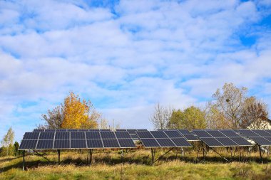Fotovoltaik hücreler, bulutlu derin mavi sonbahar gökyüzünün arka planına karşı. Sarı yapraklı ağaç. Kırsal kesimdeki güneş panelleri. Alternatif enerji kavramı