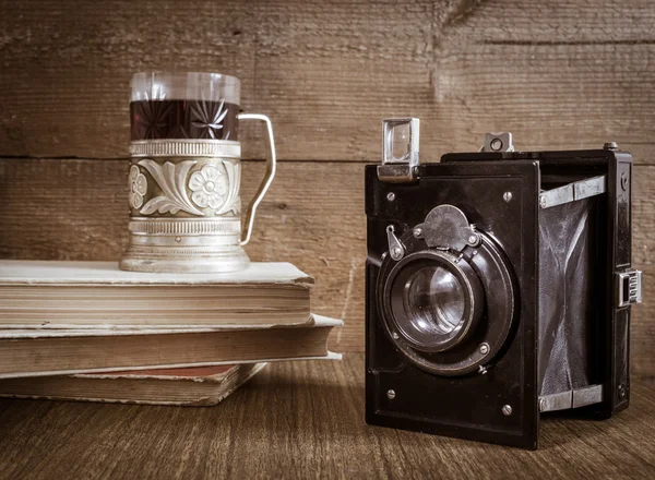 Old camera with tea in coaster and books — Stock Photo, Image