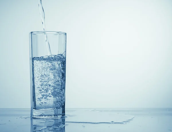 Su sıçraması ile şampanya bardağının içine beyaz zemin üzerine dökülen