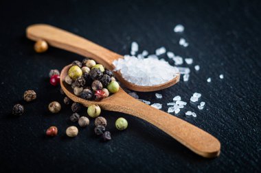 Tuz ve tam karabiber, ahşap kaşıklarda biber karışımı koyu arkaplan, üst manzara.