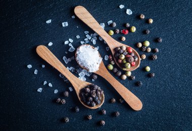 Deniz tuzu ve tüm karabiber, ahşap kaşıklarda karabiber karışımı koyu arkaplan, üst manzara.