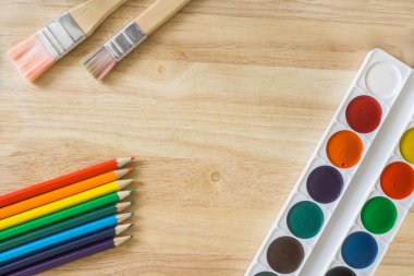Painting brushes, colored pencils and watercolor on wooden background