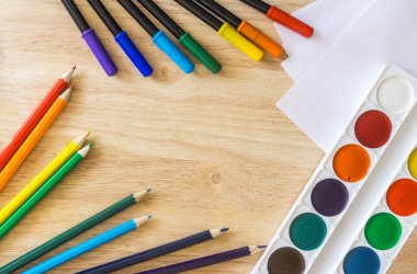 Colored felt-tip pens, lying randomly colored pencils, white paper and watercolor on wooden background