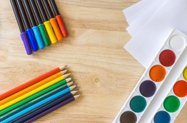 Colored pencils, lying like rainbow, white paper and watercolor on wooden background