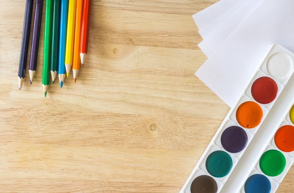 Цветные карандаши, лежащие как радуга, белая бумага и акварель на деревянном фоне — стоковое фото