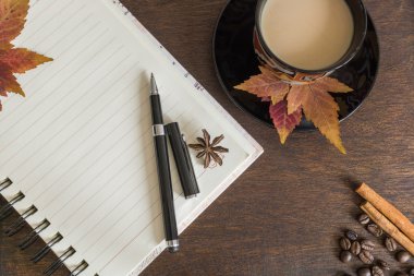 Kahve çekirdekleri, fincan kahve, sonbahar yaprakları, kalem ve defter ahşap güverte üzerinde