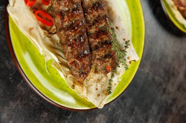 Izgara kebaplar yeşil otlar ve kırmızı biber dilimleriyle süslenmiş yassı ekmeğin üzerinde dinleniyor. Bu yemek lezzetlerin bir karışımını sergiliyor ve genel olarak çeşitli mutfaklarda kullanılıyor..