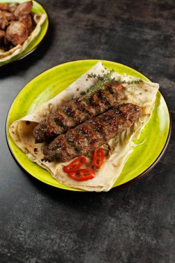 Izgara kebaplar taze yeşil bir tabakta otlu ve acılı ekmeklerin üzerine konur. Bu yemek, paylaşmak ve eğlenmek için mükemmel olan zengin bir aşçılık geleneğini ön plana çıkarıyor..