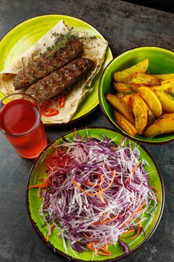Tabak vitrininde kızarmış kebap, canlı lahana salatası ve baharatlı patates dilimleri. Serinletici bir içecek kırsal bir masada yemeği tamamlar..