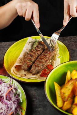 Sıradan bir lokantada salata ve patates kızartmasının renkli taraflarıyla çevrili bir ekmeğin üzerine yerleştirilmiş şişlenmiş et kesilir..