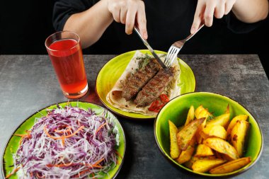 Bir insan, yanında salata ve fırında patates ile birlikte kızarmış ekmeğin üzerinde servis edilen eti de içeren bir yemeğin tadını çıkarıyor. Masada bir içki de var..