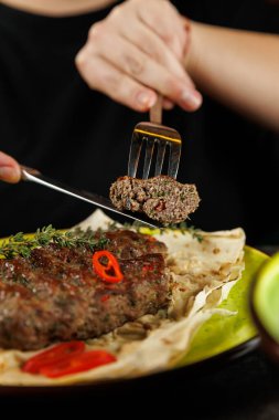 Bir insan masada otururken bir çatalla Ukrayna et tabağından bir dilim alır. Tabak taze otlar ve biberlerle süslenir, sıcak ekmek üzerine konur..