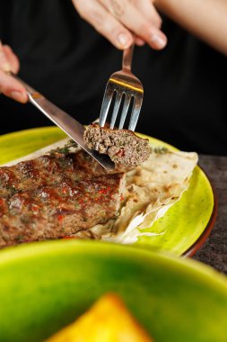 Bir insan lokantada canlı yeşil bir tabakta et dolu bir hamur işi olan kchmk 'yi kesmek için çatal ve bıçak kullanır..