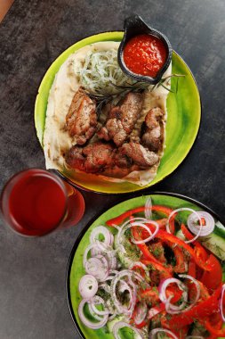 Taze hazırlanmış et, soslu ve yanında renkli bir salata ile birlikte bir ekmek üzerinde servis edilir. Bir içki yakınlarda oturur, yemek deneyimini güçlendirir..