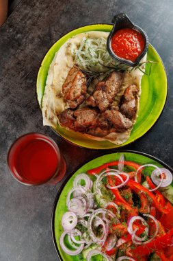 Izgara et, taze soğan salatası ve bir kase sosla birlikte yeşil bir tabakta servis edilir. Bir içki kenarda oturup, canlı bir yemek deneyimi yaratır..