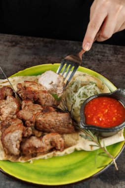 Bir insan, ekmek, salata ve sosla servis edilen ızgara eti kesmek için çatal kullanır. Bu yemek bir restoran ortamında lezzet karışımını sergiliyor..