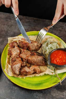 Bir insan, taze sebze ve sos ile servis edilen ızgara et tabaklarını keser. Ayarlar gündelik ve yemeğe odaklı..