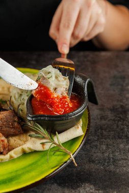 İçinde et ve sos bulunan yeşil bir tabakta servis edilir. Bir el bıçağı tutar, tabağı keser. Yemek farklı mutfaklardan gelen tatları birleştiriyor..