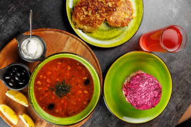 Bu sahnede farklı mutfaklardan çeşitli yemekler sergileniyor. Sebzeli bir kase çorba, krep, turşu ve renkli pancar salatası mevcut..