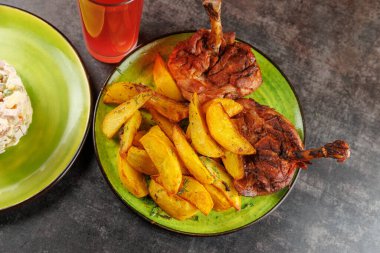 Açık yeşil bir tabakta kızarmış tavuk budu ve çıtır patates dilimleri servis edilen bir yemek. Yakınlarda renkli bir içecek duruyor, ziyafete renk katıyor..