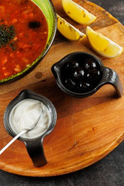 Ekşi krema ve zeytinlerle birlikte küçük kaplarda servis edilen renkli bir Ukrayna borşu. Limon, ahşap bir tahtanın üzerinde tat vermesi için duruyor..