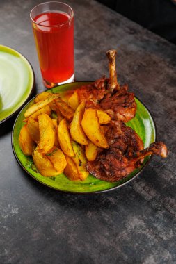 Kemikli tavuk parçaları ızgarada pişiriliyor ve yeşil tabakta kızartılmış patatesle servis ediliyor. Sıcak bir mekanda bir bardak kırmızı içecek yemeğe eşlik eder..