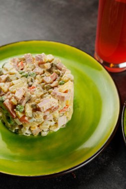 Sebze ve etlerden yapılmış geleneksel bir Ukrayna salatası bir bardak kırmızı içecekle birlikte yeşil bir tabağın üzerinde oturur. Canlı düzenleme kültürel tatları vurguluyor.