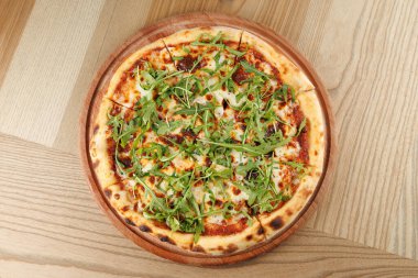 Altın hamurlu yuvarlak bir pizza erimiş peynir ve zengin domates sosu içerir. Kırsal ahşap bir tabakta taze roka ile cömertçe süslenmiştir..