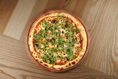 Taze pişmiş pizza, üzerinde peynir ve yeşillikler olan ahşap bir tabakta oturur. Kırsal ahşap bir masaya yerleştirilir ve yemek yemek için mükemmel bir yemek sahnesi yaratır..