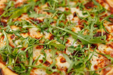 Taze pişmiş bir pizza erimiş peynir ve canlı roka yapraklarıyla kaplıdır. Bu yemek bir ev mutfağında pizza yapma sanatını sergiliyor..