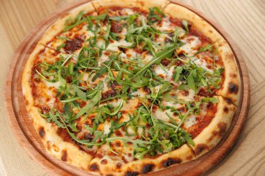 Yeni pişmiş bir pizza, eritilmiş peynir, domates sosu ve canlı yeşil roka yapraklarının sergilendiği ahşap servis tahtasının üzerinde duruyor. Arkadaşlar masanın etrafında toplanın ve tadını çıkarın..