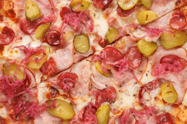Pizza dilimleri, jambon, salam, turşu ve pembe soğan malzemelerini gösteriyor. Ekmek kabuğu altın sarısı ve peynir erimiş. Arkadaşlar arasında paylaşmak için mükemmel bir yemek..