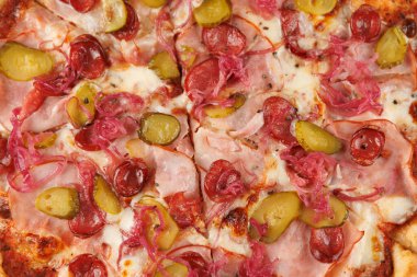 Taze bir pizza ahşap bir masada jambon, turşu ve soğanla hazırlanır. Renkli malzemeler bu yemeği davetkar ve arkadaşlarla yemek için mükemmel yapıyor..