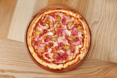 Etli ve turşulu lezzetli bir pizza sıradan bir yemek alanında ahşap bir tabakta oturur. Kabuk altın ve çıtır çıtır, herkesi paylaşmaya ve eğlenmeye davet ediyor..