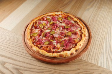 Birkaç lezzetli yemek ahşap bir masada çeşitli mutfakların altını çiziyor. Etli, turşulu ve domatesli yeni pişmiş bir pizzaya odaklanıyoruz..