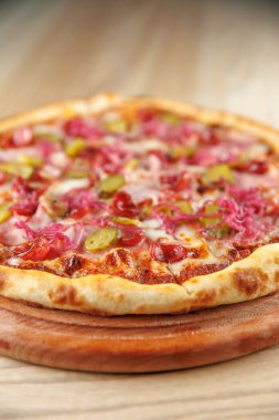 Peynirli, pepperonili, turşulu, soğanlı ve biberli bir pizza bir restoran ortamında ahşap bir tahtaya yerleştirilir. Yemek, bir öğünde çeşitli tatlar sunar..
