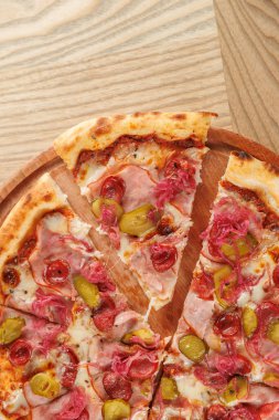 Pizza dilimleri yuvarlak ahşap bir tahta üzerinde düzenlenir. Pizzada jambon, turşu ve çeşitli malzemeler var. Öğle veya akşam yemeği için arkadaşlarla paylaşılmaya hazır..