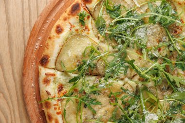 Düz ekmek ince dilimlenmiş patateslerle, taze yeşil otlarla ve tahtadan yapılmış peynirle kaplıdır. Bu yemek, klasik bir mutfağın çeşitli lezzetlerini ön plana çıkarıyor..