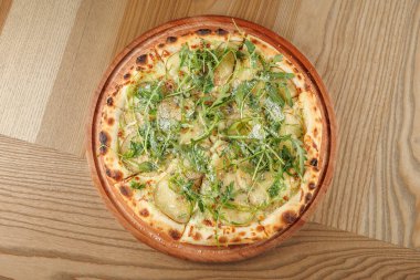 Pizza taze sebzeler, dilimlenmiş sebzeler ve rendelenmiş peynirle kaplı ince bir kabuğa sahiptir. Ahşap aksanlı bir restoranın tahta tahtasında servis ediliyor..