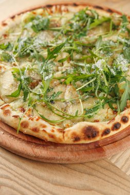 Taze bir pizza, ahşap bir tahtaya yerleştirilmiş roka ve peynirle kaplı ince bir kabuğa sahiptir. Bu yemek, öğle yemeği saatinde arkadaşça yenmeye hazır..