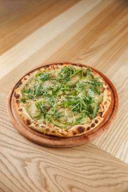 Tahta servis tahtasında taze yeşillikle kaplanmış ahşap kaplı pizza sunuluyor. Bu yemek basit malzemeler sergiliyor ve sıradan bir yemek deneyiminin parçası..