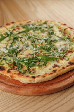 Taze roka ve erimiş peynirle kaplı bir ekmek ahşap bir tahtanın üzerinde duruyor. Ayarlar, rahat bir ortamda keyifli bir yemek olduğunu gösteriyor..