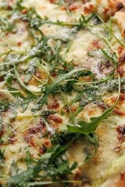 Lezzetli bir pizza taze pişmiş, eritilmiş peynir ve bir kat taze roka ile kaplıdır. Sahnede sıcaklık ve tatlarla dolu bir ev mutfağı sergileniyor..