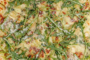 Taze pizza, erimiş peynir ve canlı roka ile kaplı bir masada oturur. Tabakta kabuklu bir taban sergileniyor ve içinde çeşitli tatlar var. Herkesi bir lokma yemeye davet eder..