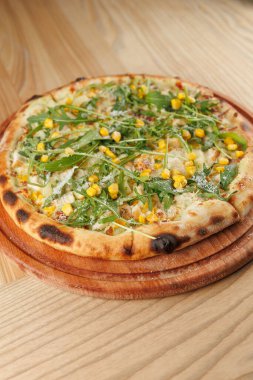 Mısır ve roka ile taze pişmiş bir pizza ahşap servis tahtasına yerleştirilir. Dekor, ahşap mobilyaları olan, rahat bir atmosferi davet eden sıradan bir yemek yeri..