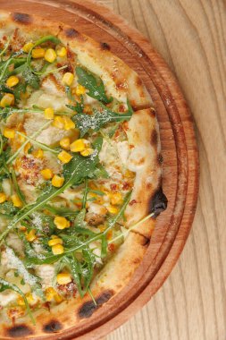 İnsanlar taze pişmiş bir pizzayı paylaşmak için bir masanın etrafında toplanırlar. Pizzada tatlı mısır ve taze roka var. Sıcak, davetkar atmosfer güzel anları teşvik eder..