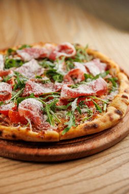 Tahta bir tahtanın üzerinde et, taze yeşillik ve peynirli pizza dilimleri servis edilir. Pizza yeni pişmiş ve sıradan bir yemek ortamında eğlenmeye hazır..