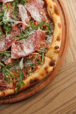 Taze pişmiş pizza dilimleri ve üzerine peynir serpiştirilmiş roka. Bu tabak yuvarlak bir tahta üzerinde servis edilir. Sıradan bir yemeği paylaşmak için mükemmel..