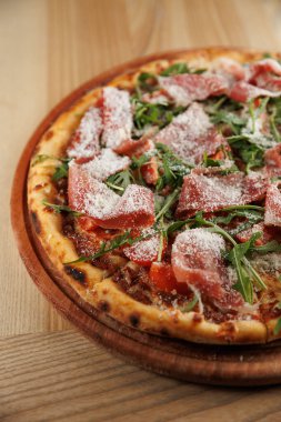 Lezzetli bir pizza malzemesi, üzerine peynir serpiştirilmiş taze et ve sebzeler serpiştirilmiş. Sıcak bir restoran ortamında ahşap bir tahtada servis edilir..