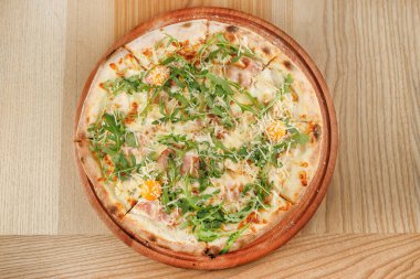 Ahşap bir yüzeye yerleştirilmiş yuvarlak bir pizza roka, peynir ve et parçalarıyla kaplıdır. Ayarlama yerel bir lokantada gündelik bir yemek deneyimi içeriyor..